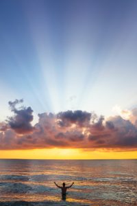 man raising his arms on sea under black clouds